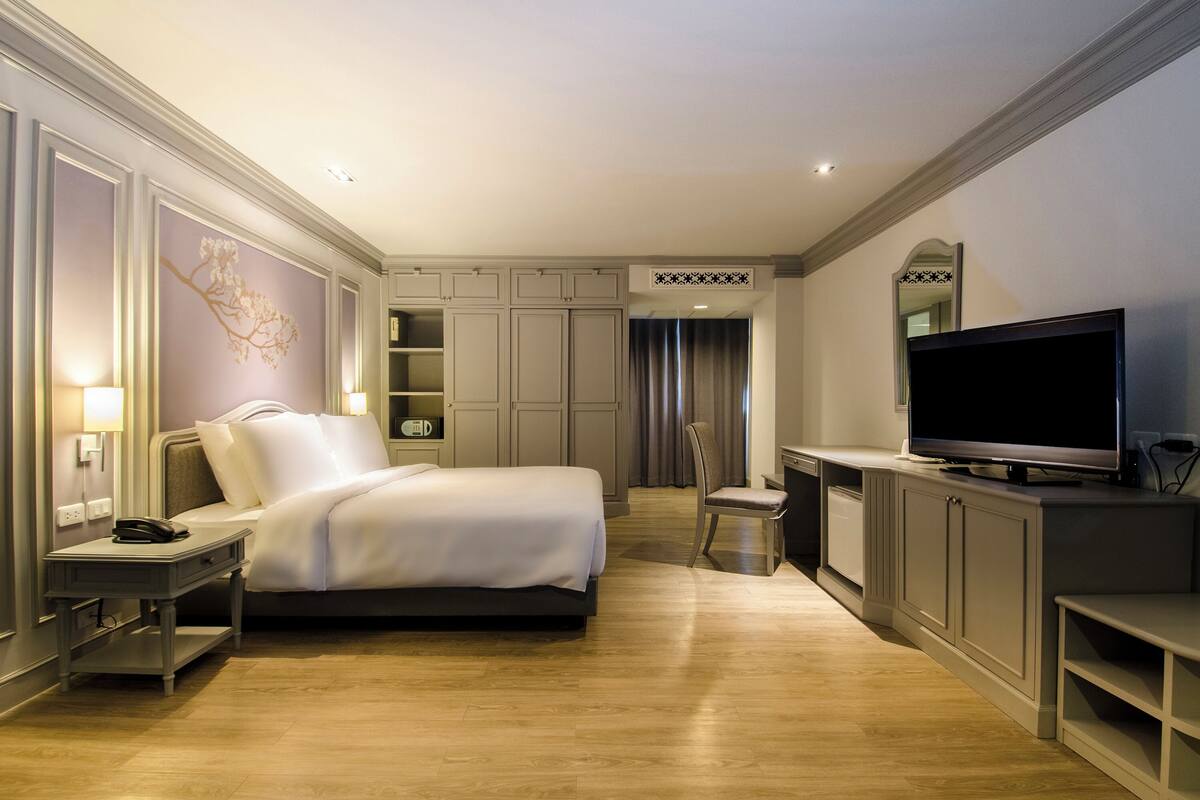 A hotel room with a bed, bedside table, lamp, TV, and built-in cabinets.
