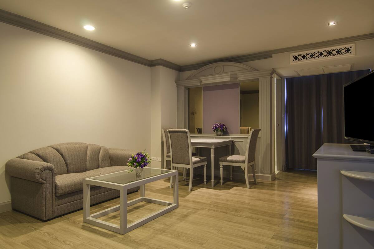 A modern living room with a sofa, a glass coffee table, and a dining area with chairs and a table.