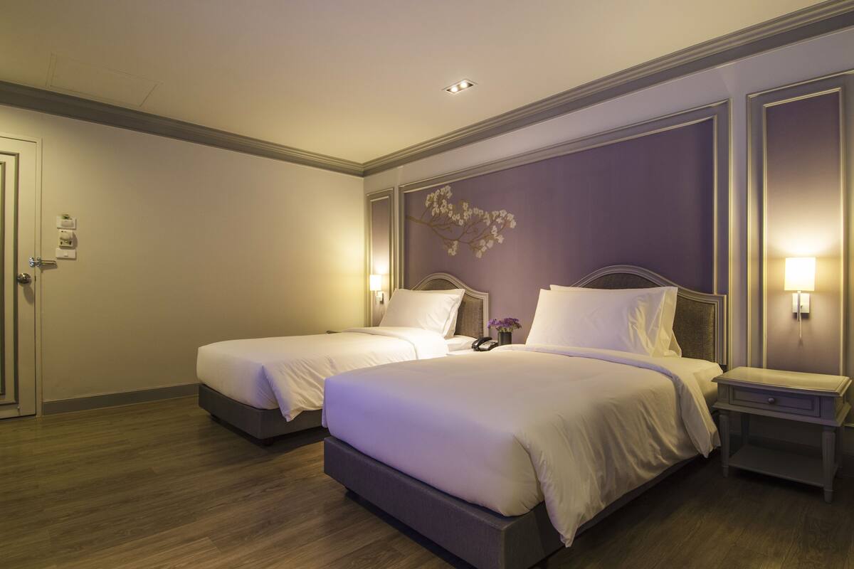 A hotel room with two beds, a nightstand, and a wall-mounted lamp.