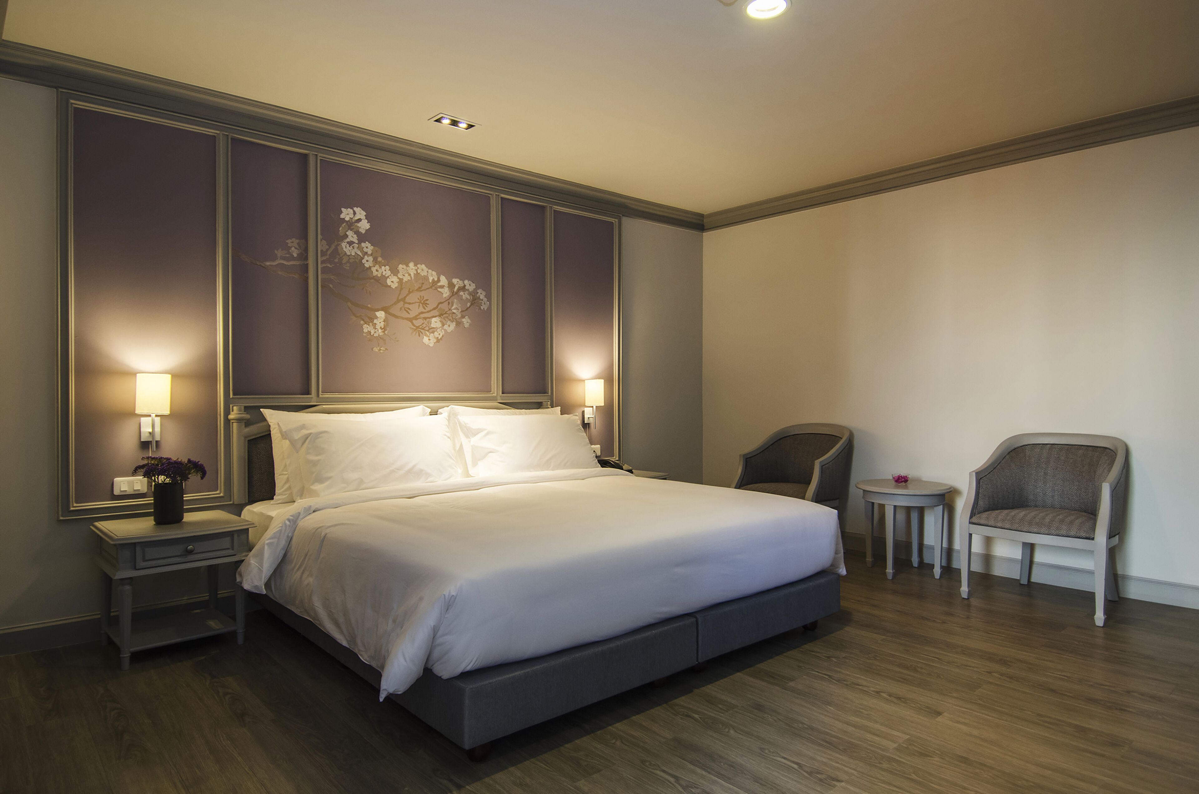 A neatly made bed with a headboard, two bedside tables with lamps, a small round table, and a chair.