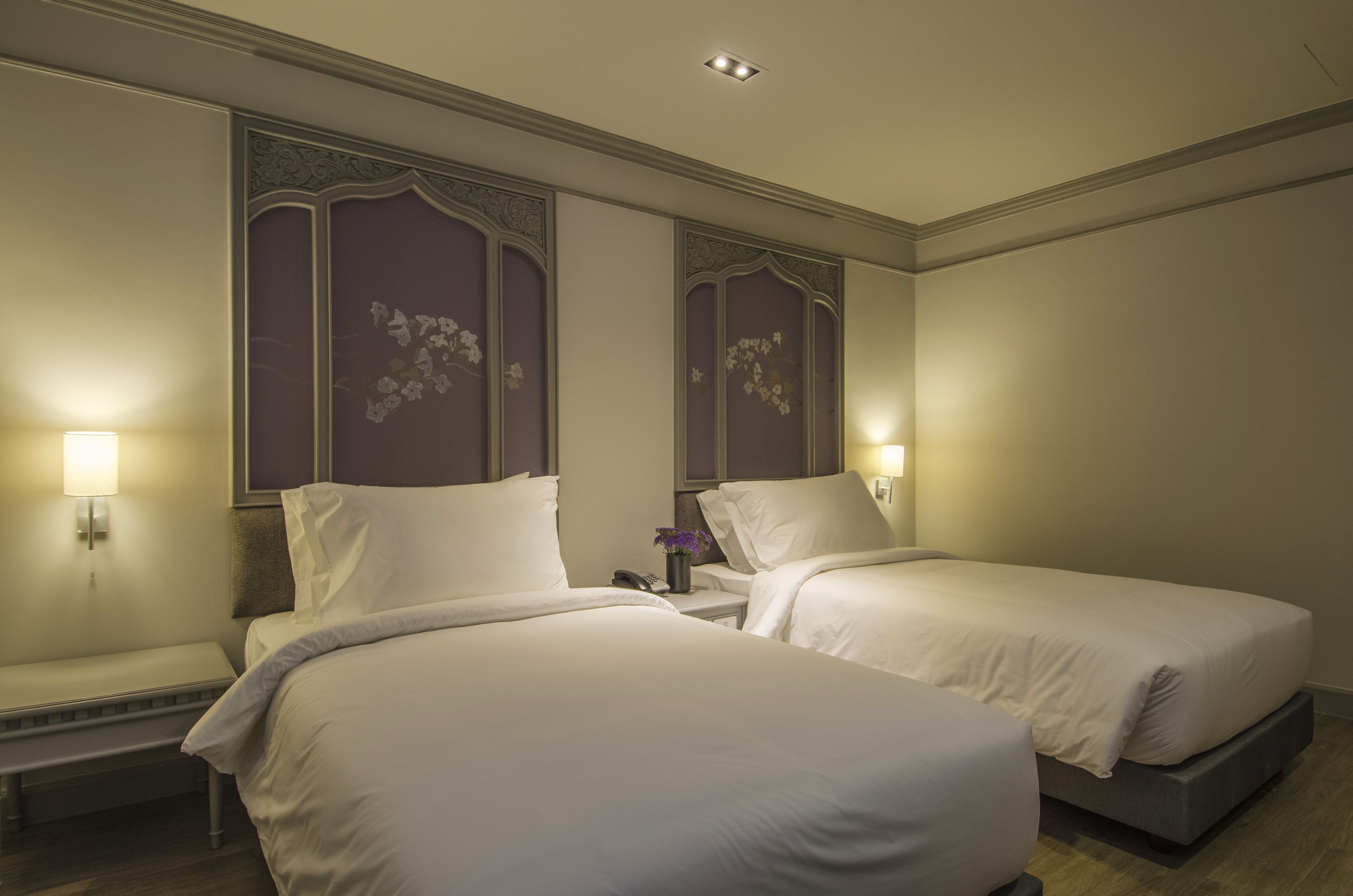 A hotel room with two beds, a bench, and a nightstand with a lamp.