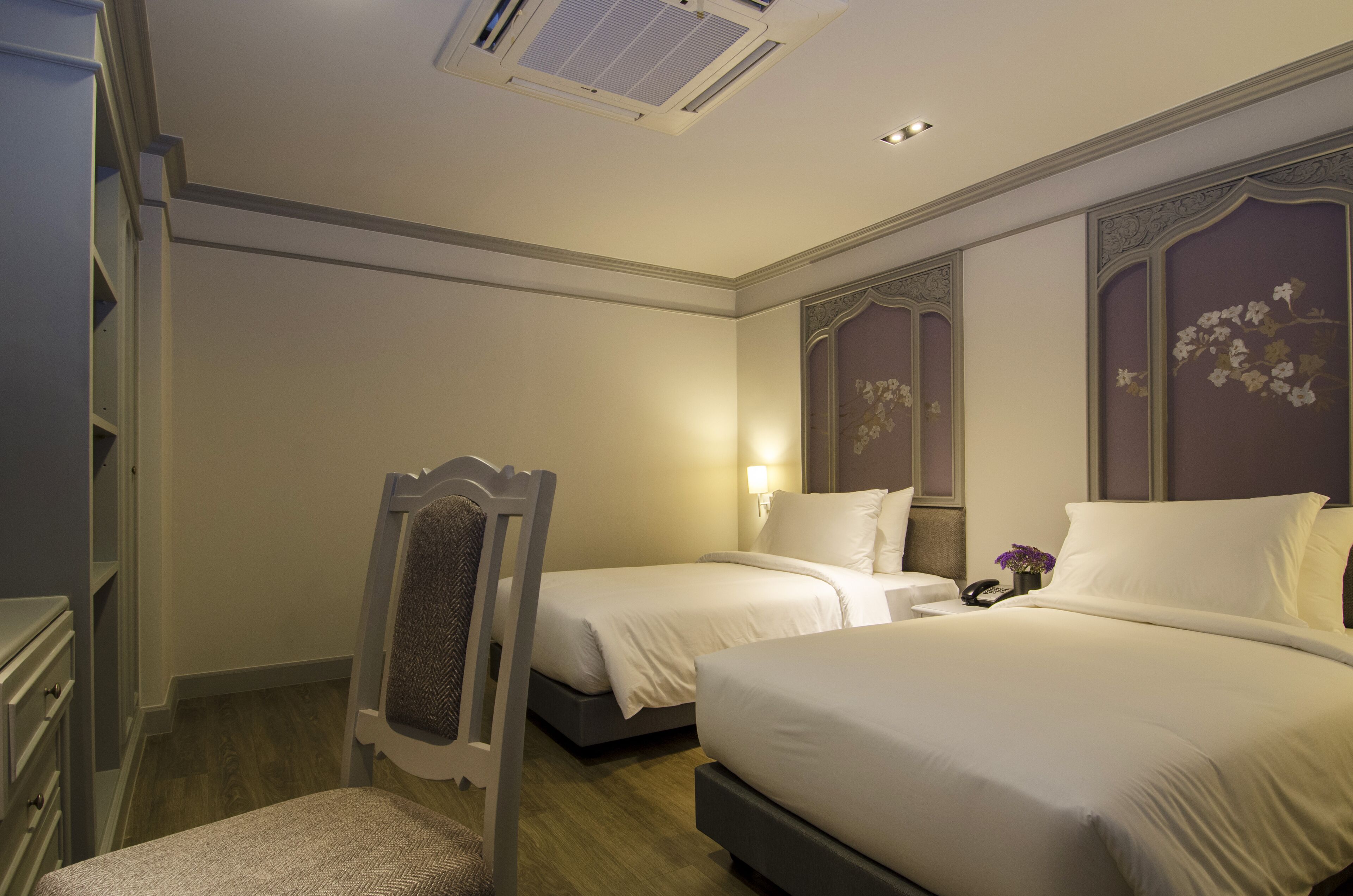 A hotel room with two beds, a wardrobe, a chair, and a bedside table with a lamp.