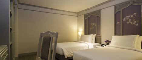 A hotel room with two beds, a wardrobe, a chair, and a bedside table with a lamp.
