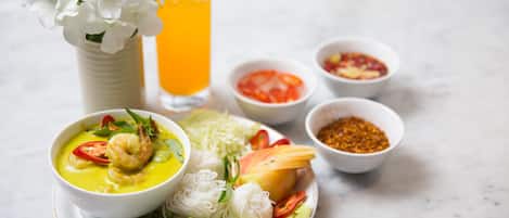 Prato de comida com uma tigela de sopa, um copo de suco de laranja e diversos acompanhamentos.