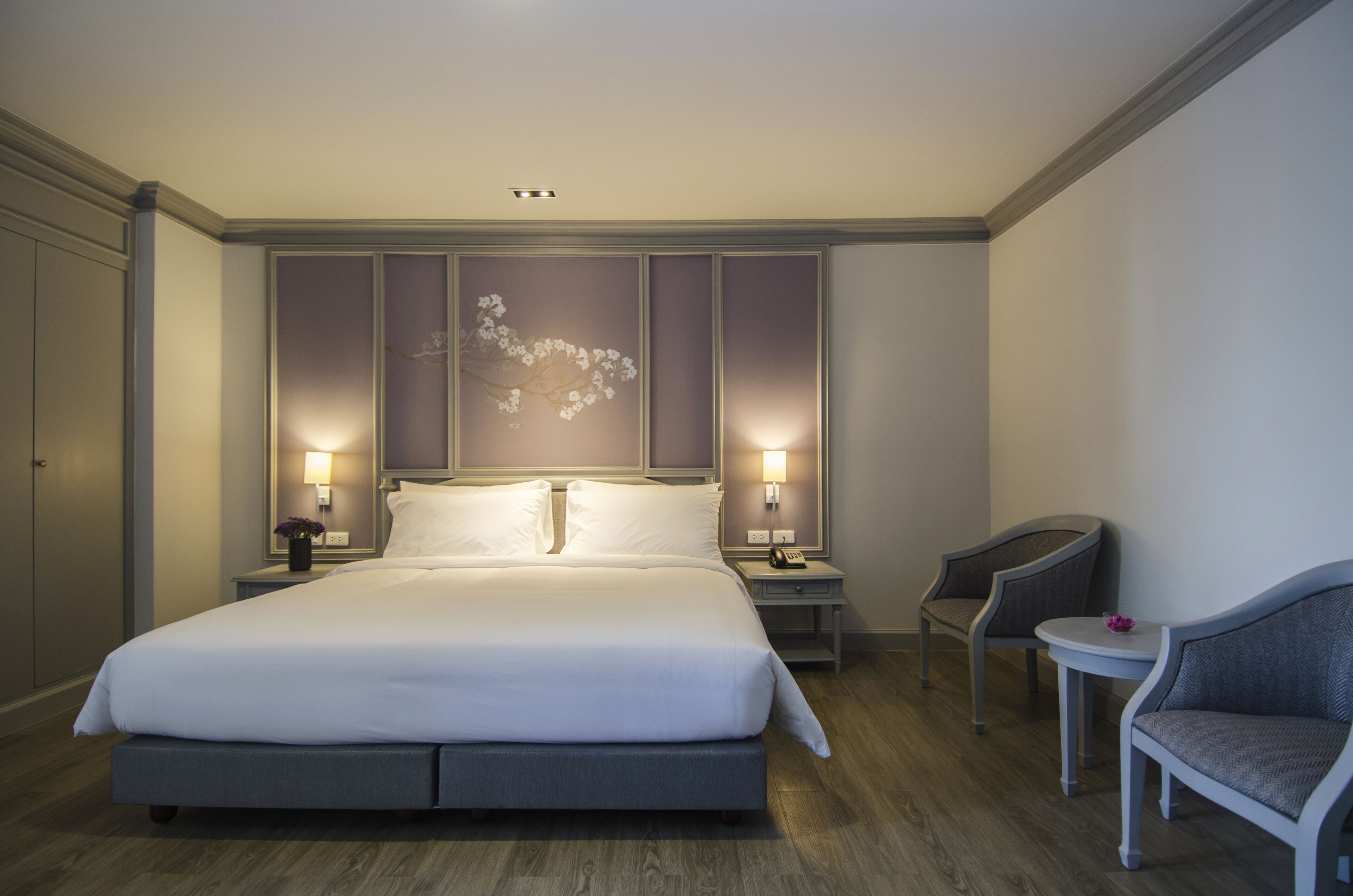 Ein Hotelzimmer mit einem großen Bett, zwei Nachttischen mit Lampen, einem kleinen runden Tisch mit einem Stuhl und einer dekorativen Wandverkleidung.