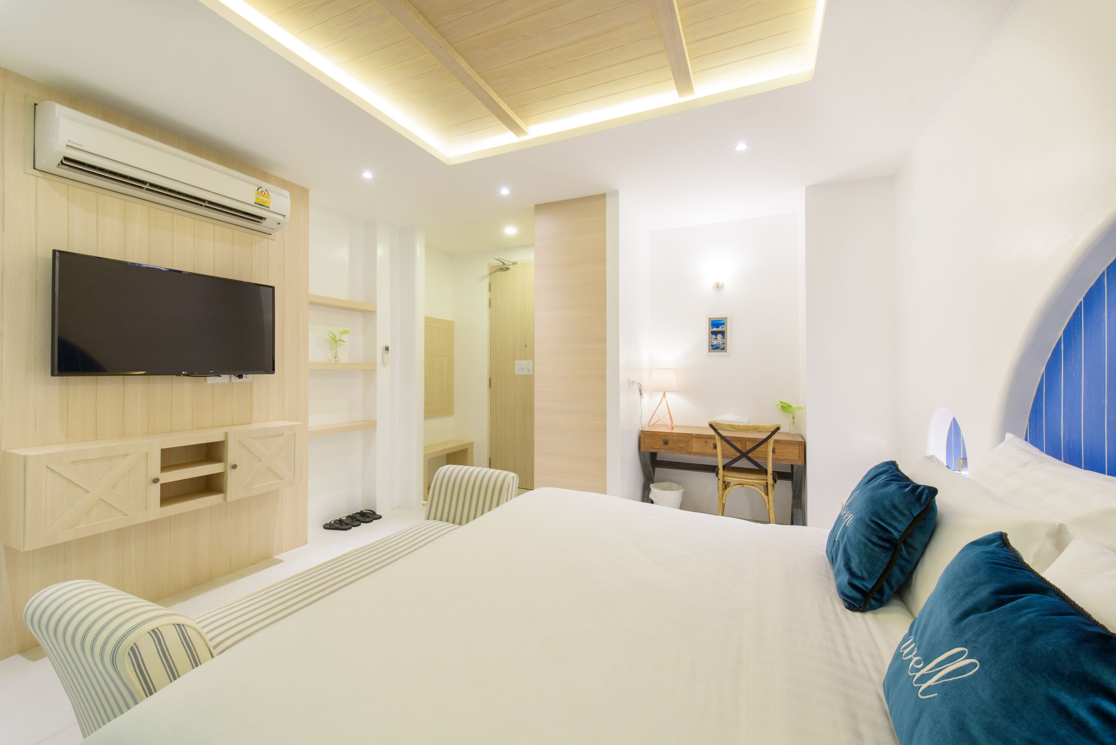 A modern hotel room with a large bed, a desk, a television, and a ceiling light fixture.