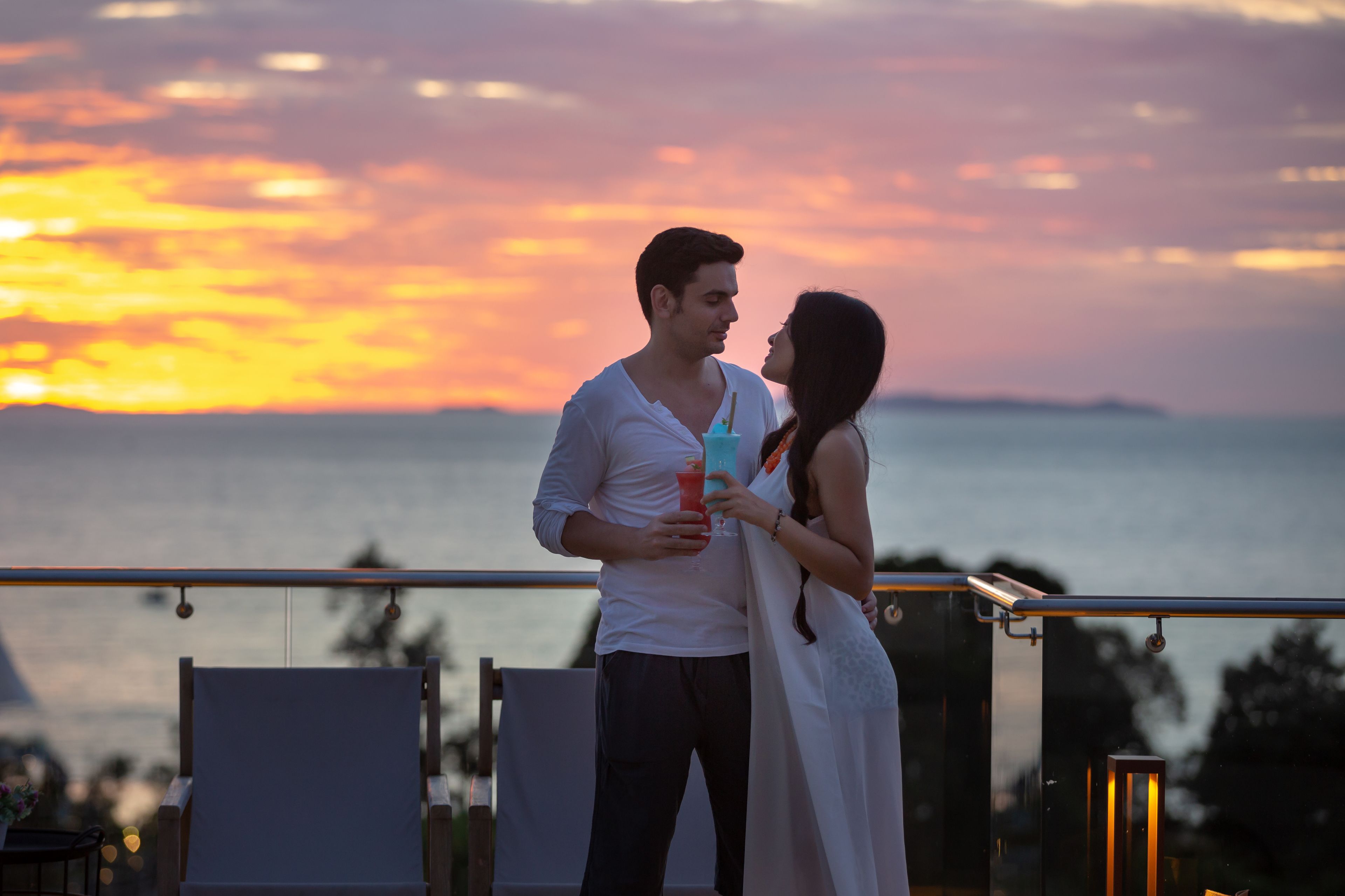 Una pareja está de pie en un balcón con vista al atardecer.