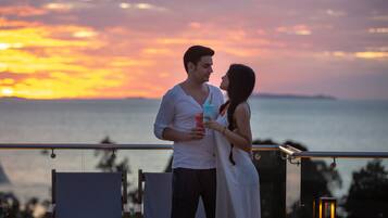 Una pareja está de pie en un balcón con vista al atardecer.