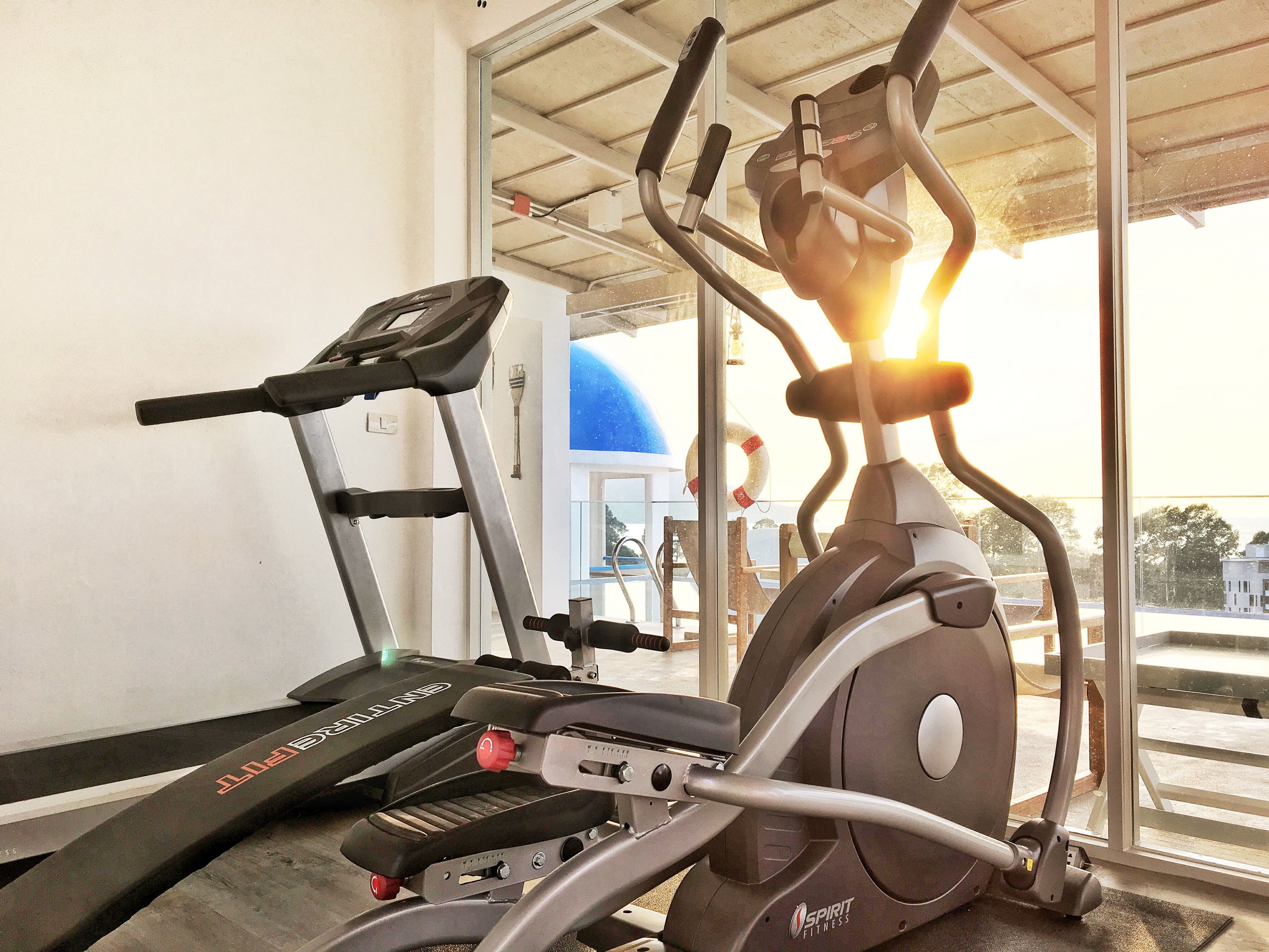 A gym with stationary bikes and treadmills, large windows, and a view of the outside.