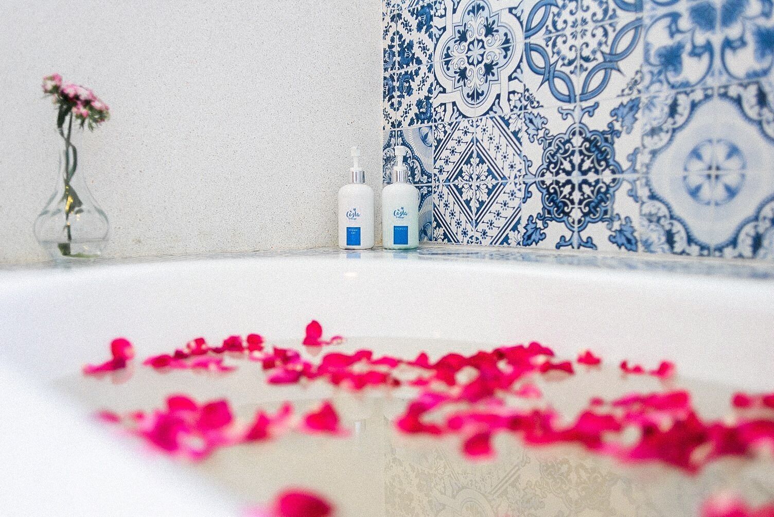 Una bañera con pétalos de rosa, dos botellas de loción y un florero con flores.