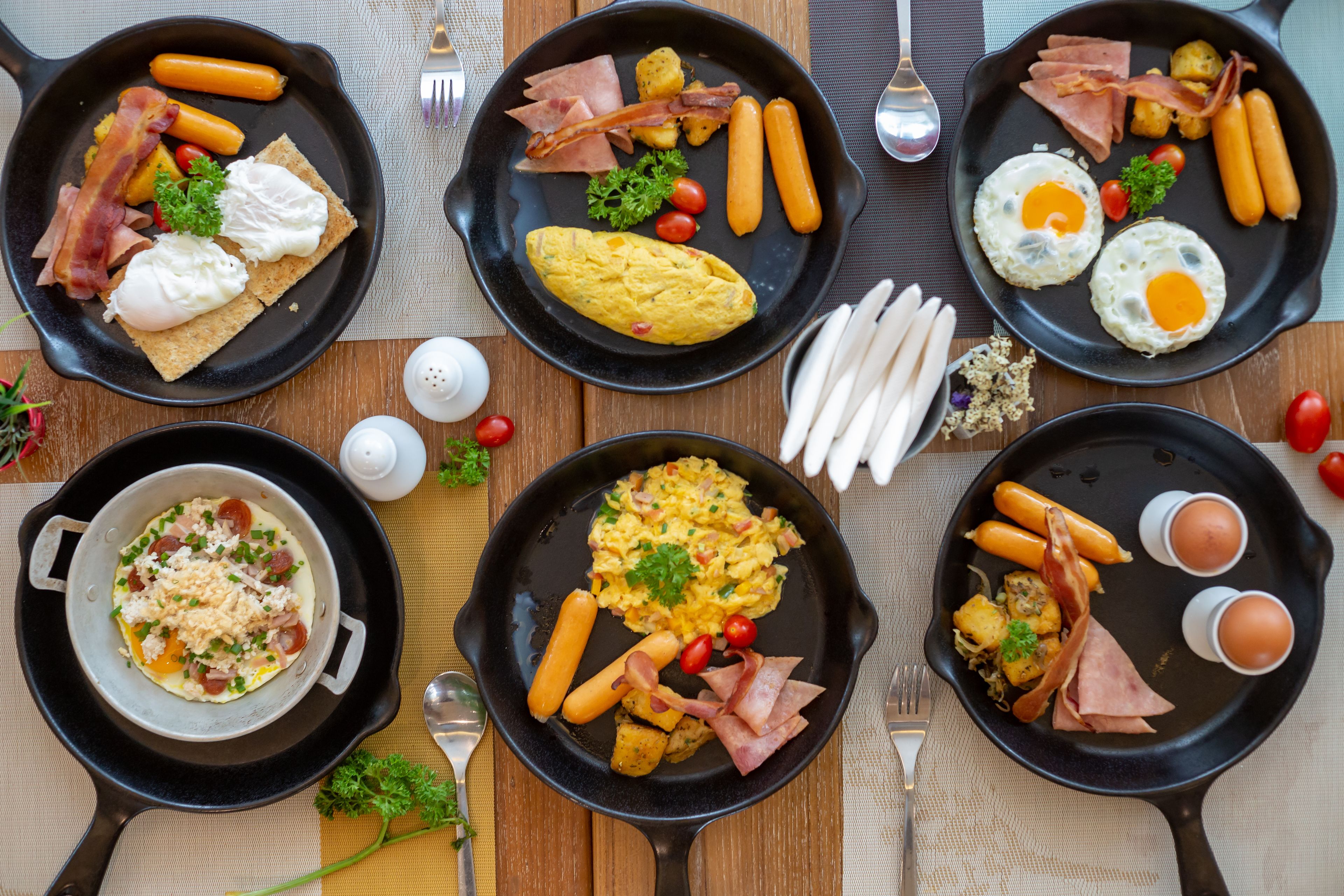 A breakfast spread with various dishes including eggs, bacon, sausages, and toast on a wooden table.