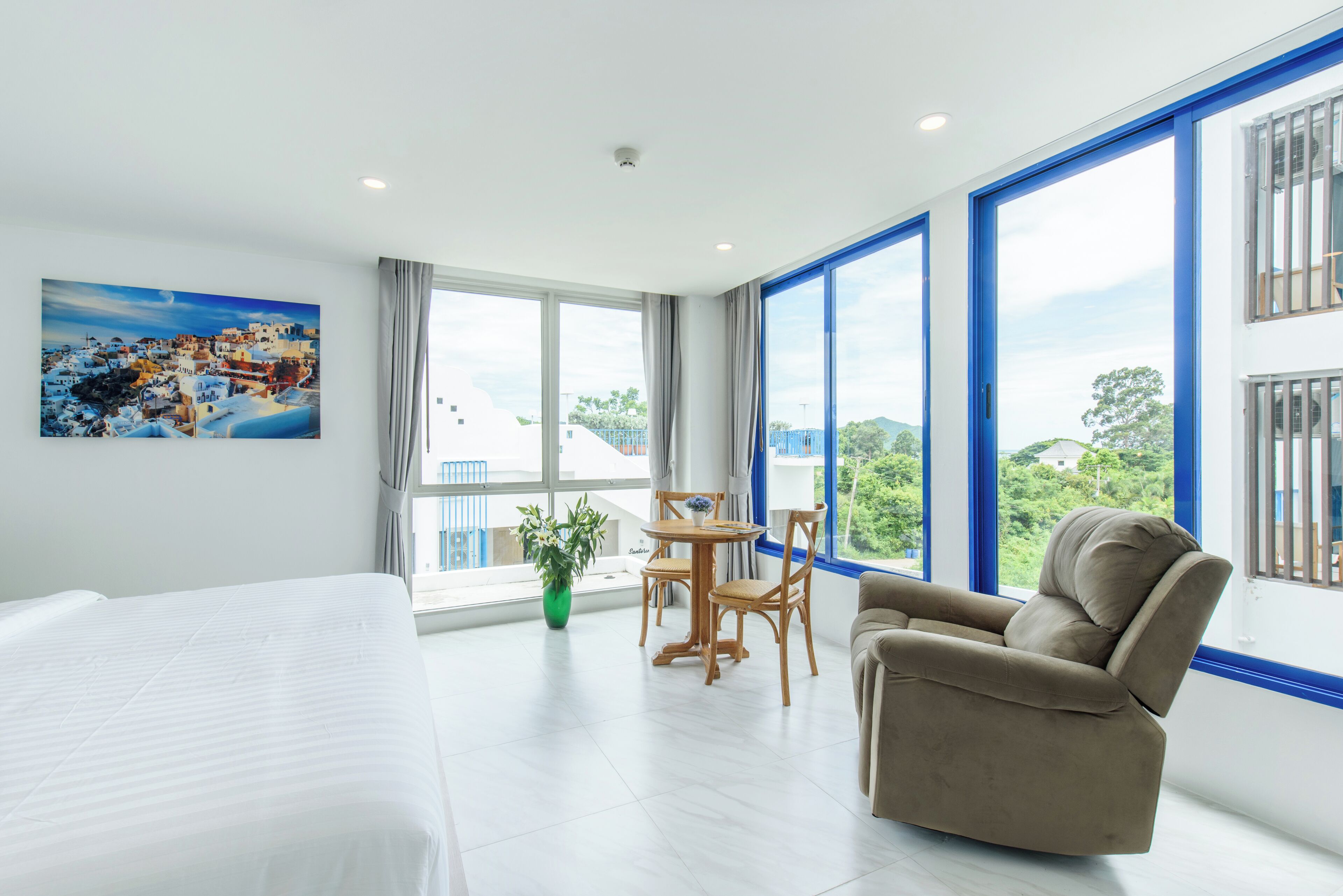 Habitación de hotel con cama, sofá, mesa de comedor con sillas y ventanas amplias con vista a la ciudad.