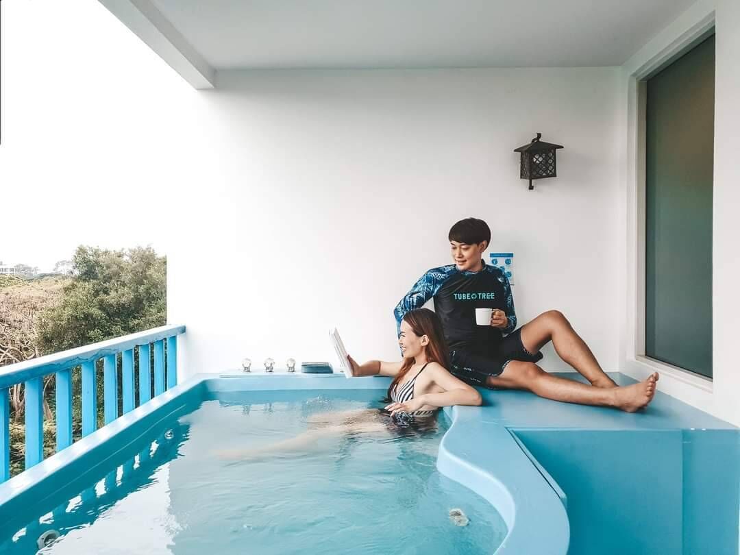A person sitting on a pool edge, another person in the water, and a small pool with a blue edge.