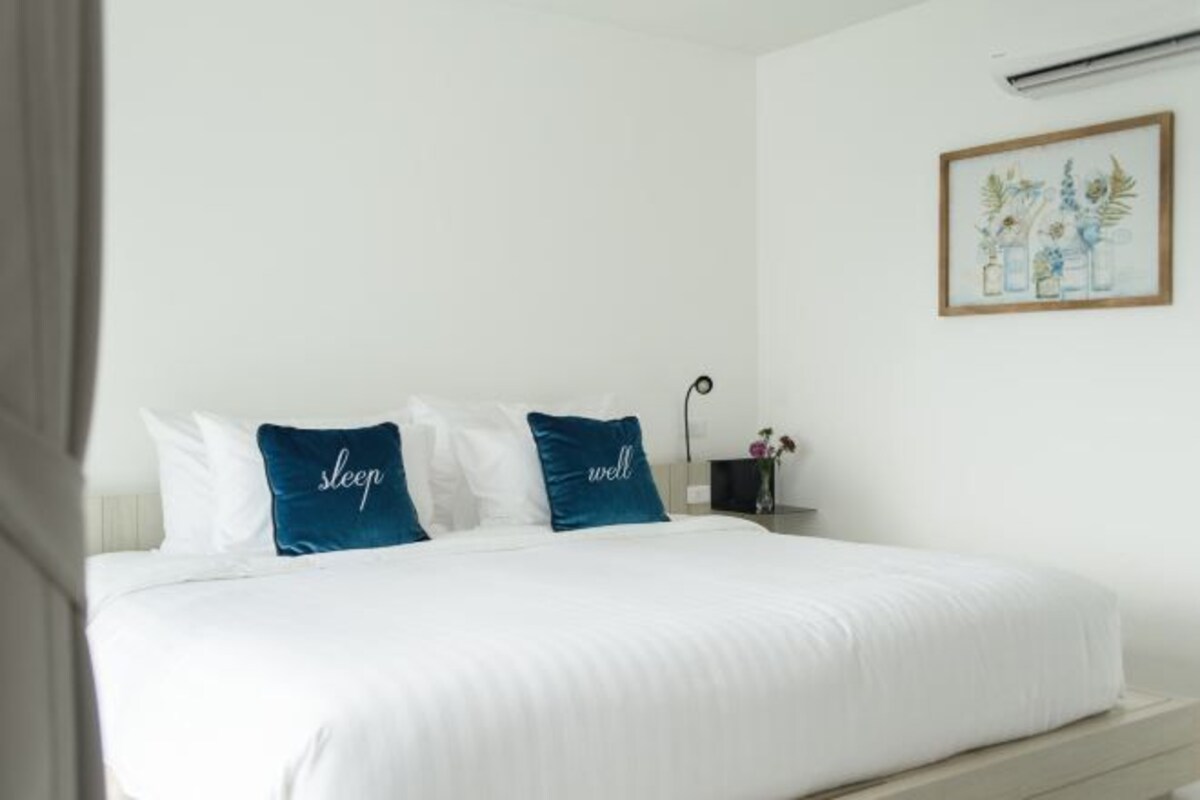 A neatly made bed with white bedding and two blue pillows with the words "sleep" and "well" on them.