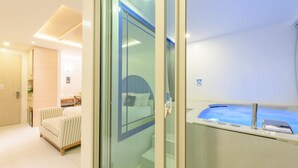 Ein modernes Hotelzimmer mit Glastür zu einem Badezimmer mit Badewanne.