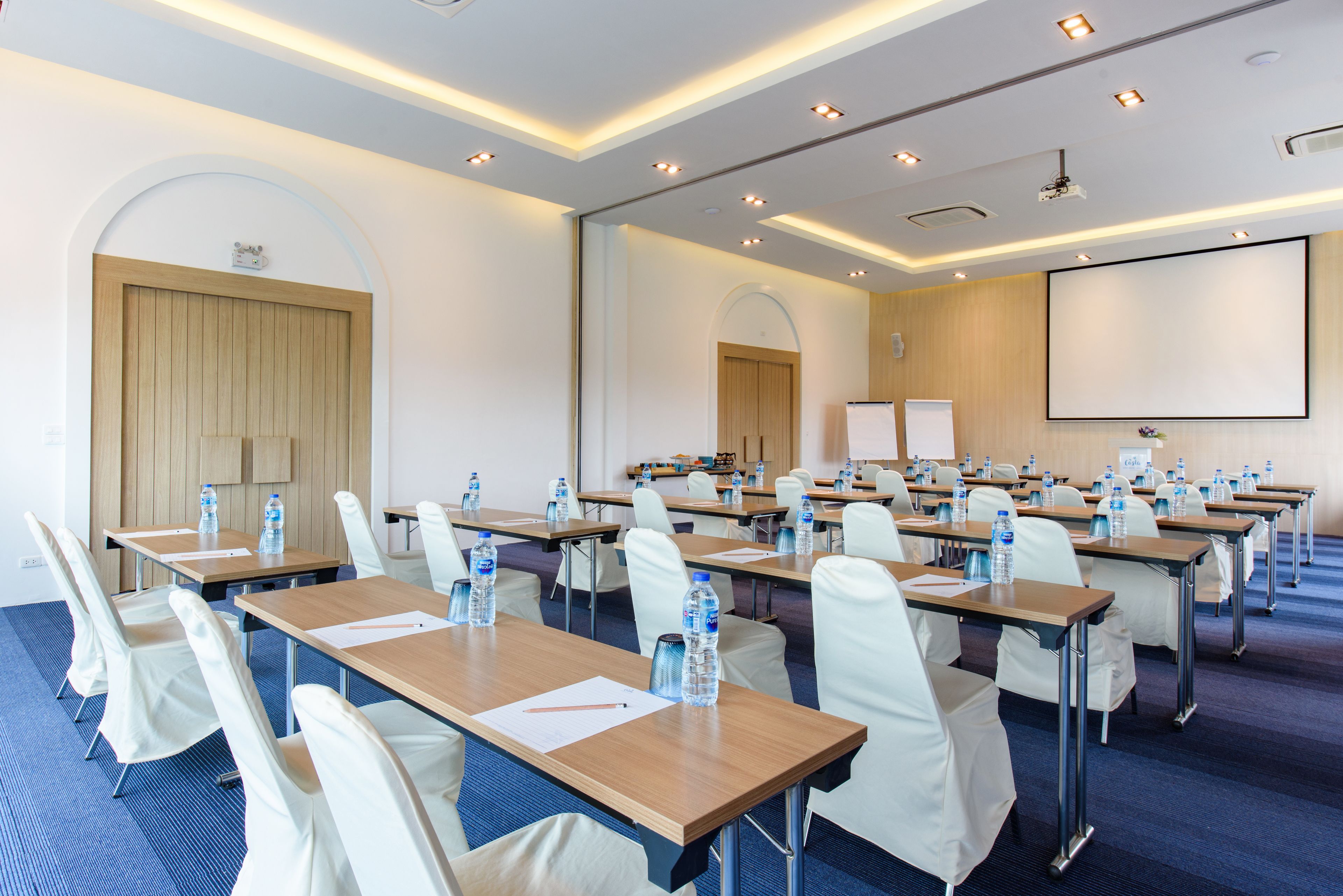 A conference room with rows of tables, chairs, and a projector screen.