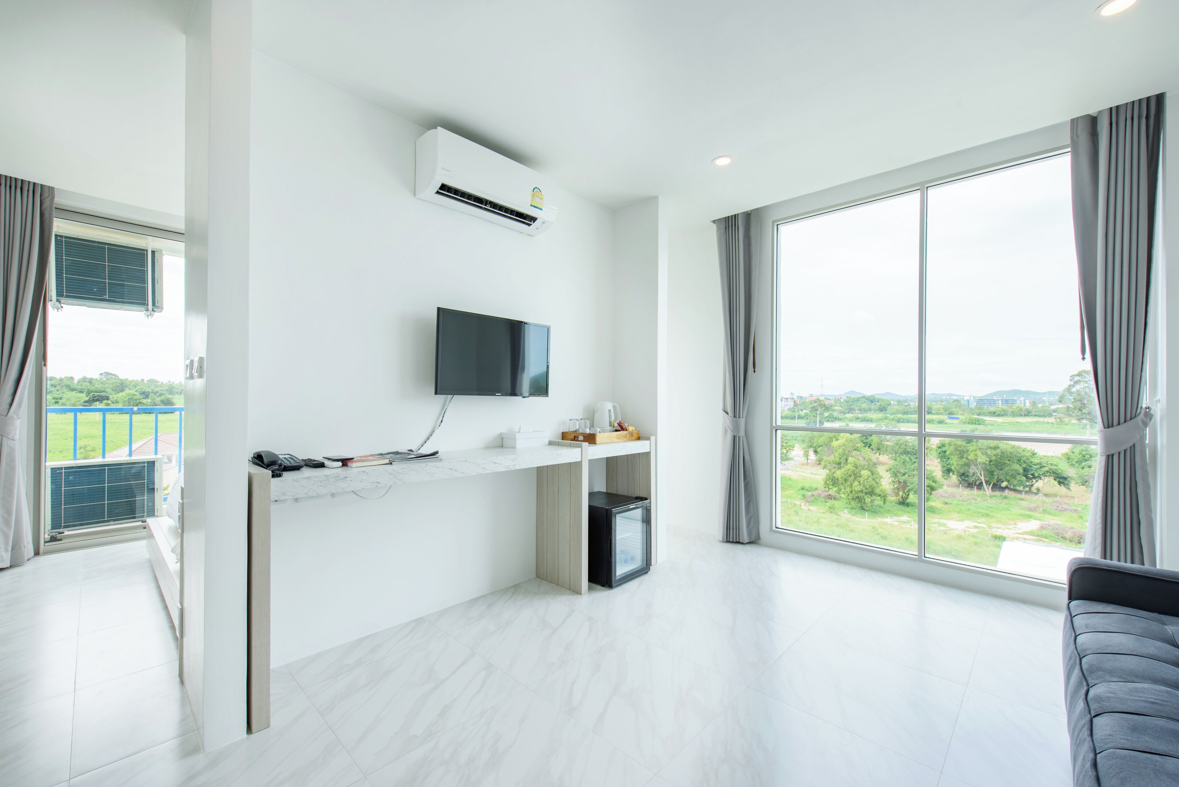 Una sala de estar moderna con un ventanal grande, un televisor de pantalla plana, una pequeña cocina y un sofá gris.