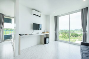 Una sala de estar moderna con un ventanal grande, un televisor de pantalla plana, una pequeña cocina y un sofá gris.