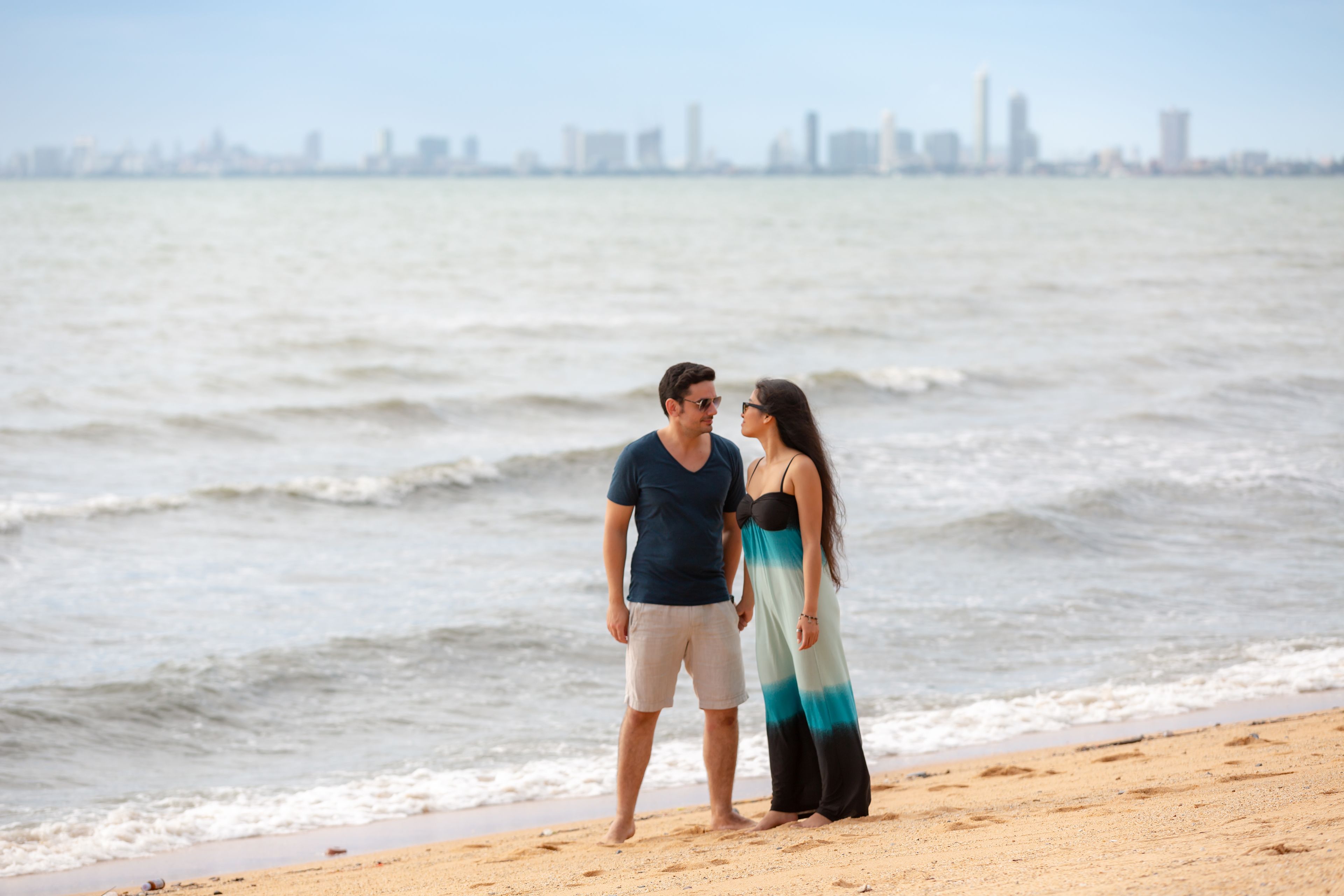 Una pareja está de pie en la playa, con el horizonte de una ciudad al fondo.