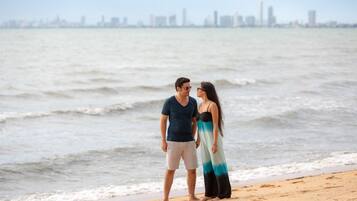 Una pareja está de pie en la playa, con el horizonte de una ciudad al fondo.