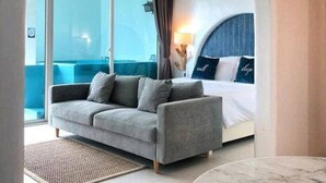 Ein modernes Hotelzimmer mit einer Couch, einem Bett, einem Marmortisch und Blick durch eine Glastür.