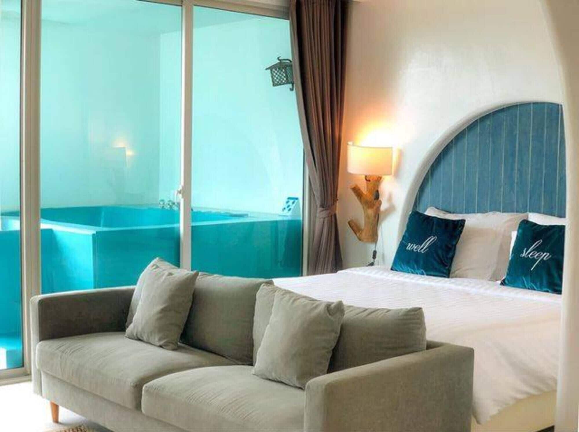 A hotel room with a bed, a sofa, a bathtub, and a view of the sea.