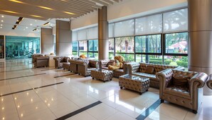 A spacious lobby with leather sofas and ottomans arranged in a row, large windows offering views of greenery, and a modern ceiling design. - Marble Garden View Pattaya (Pattaya)