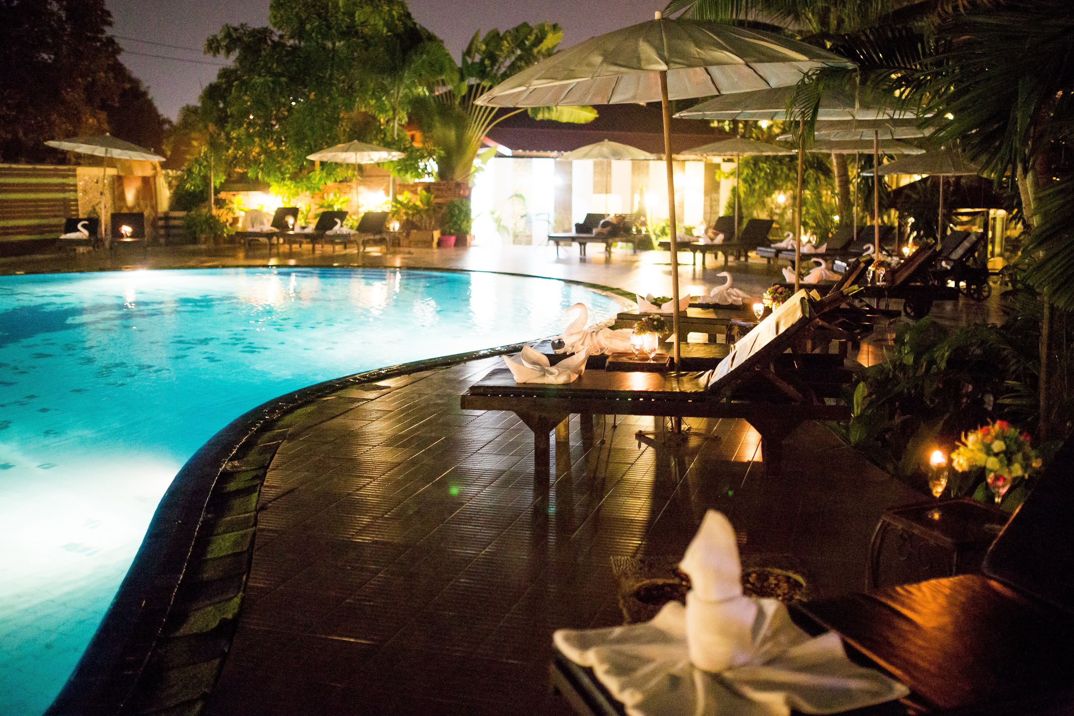 A poolside area with lounge chairs and umbrellas, surrounded by lush greenery.
