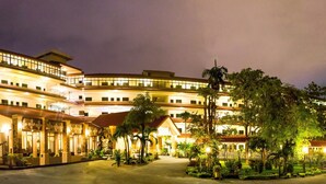 A multi-story hotel with a curved facade, multiple balconies, and a well-lit entrance area with palm trees. - Marble Garden View Pattaya (Pattaya)