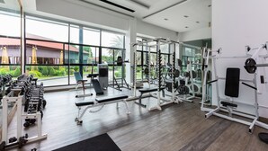 A modern gym with various weightlifting equipment, large windows, and a view of greenery outside. - Marble Garden View Pattaya (Pattaya)