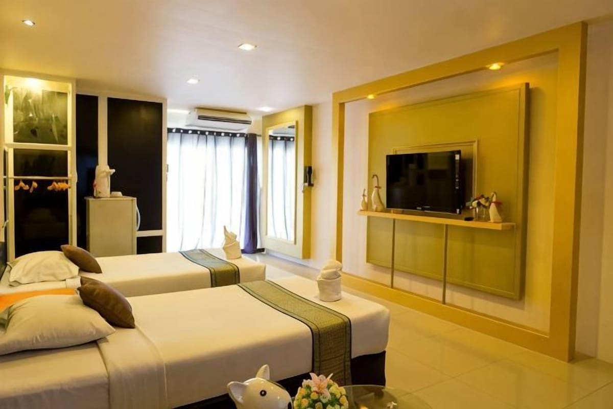 A hotel room with two beds, a TV, a mirror, and a window with curtains.