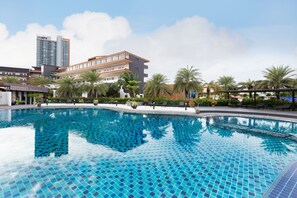 Piscina com azulejos azuis, cercada por palmeiras e edifícios modernos.