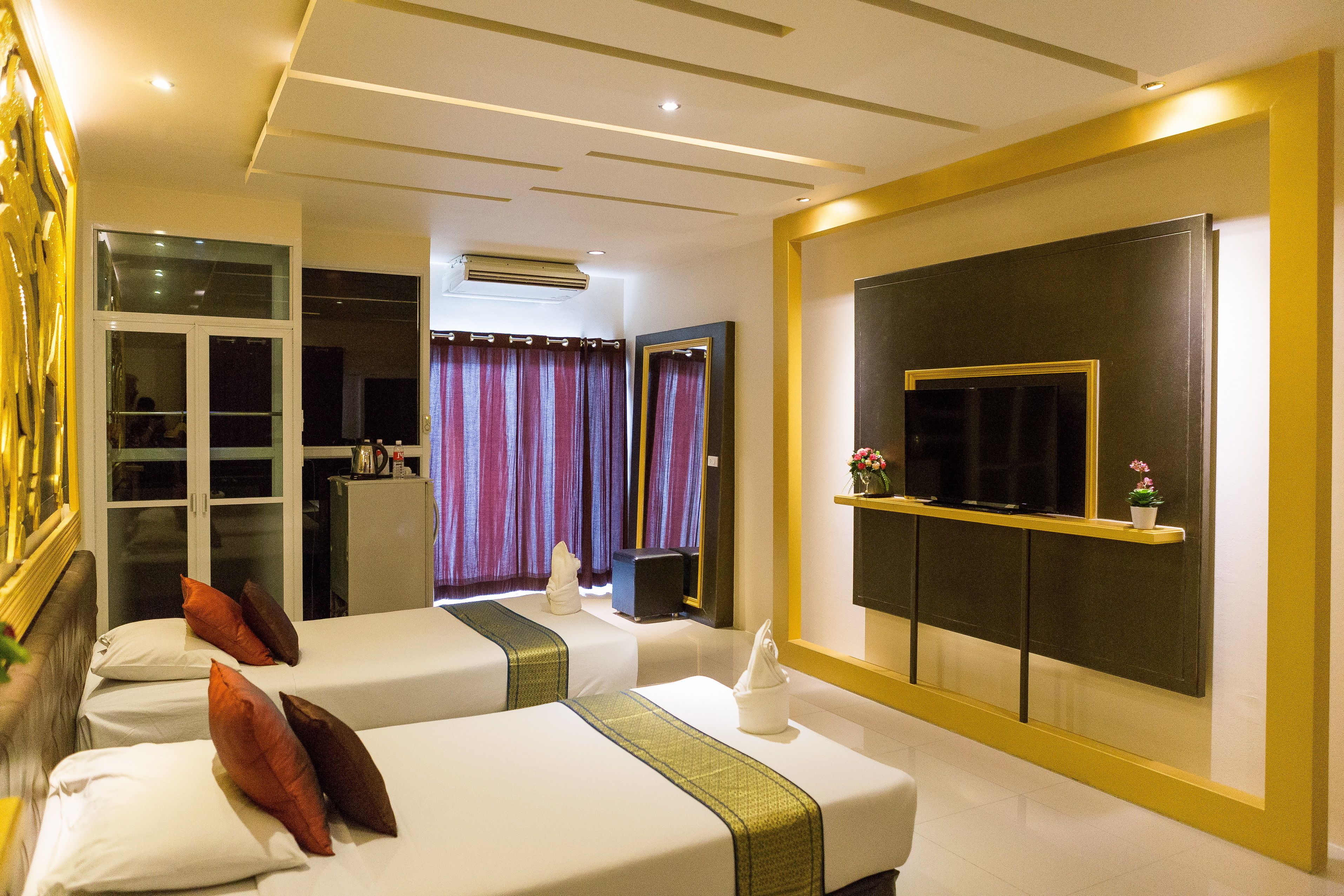 A hotel room with two beds, a TV, a mirror, and a window with curtains.