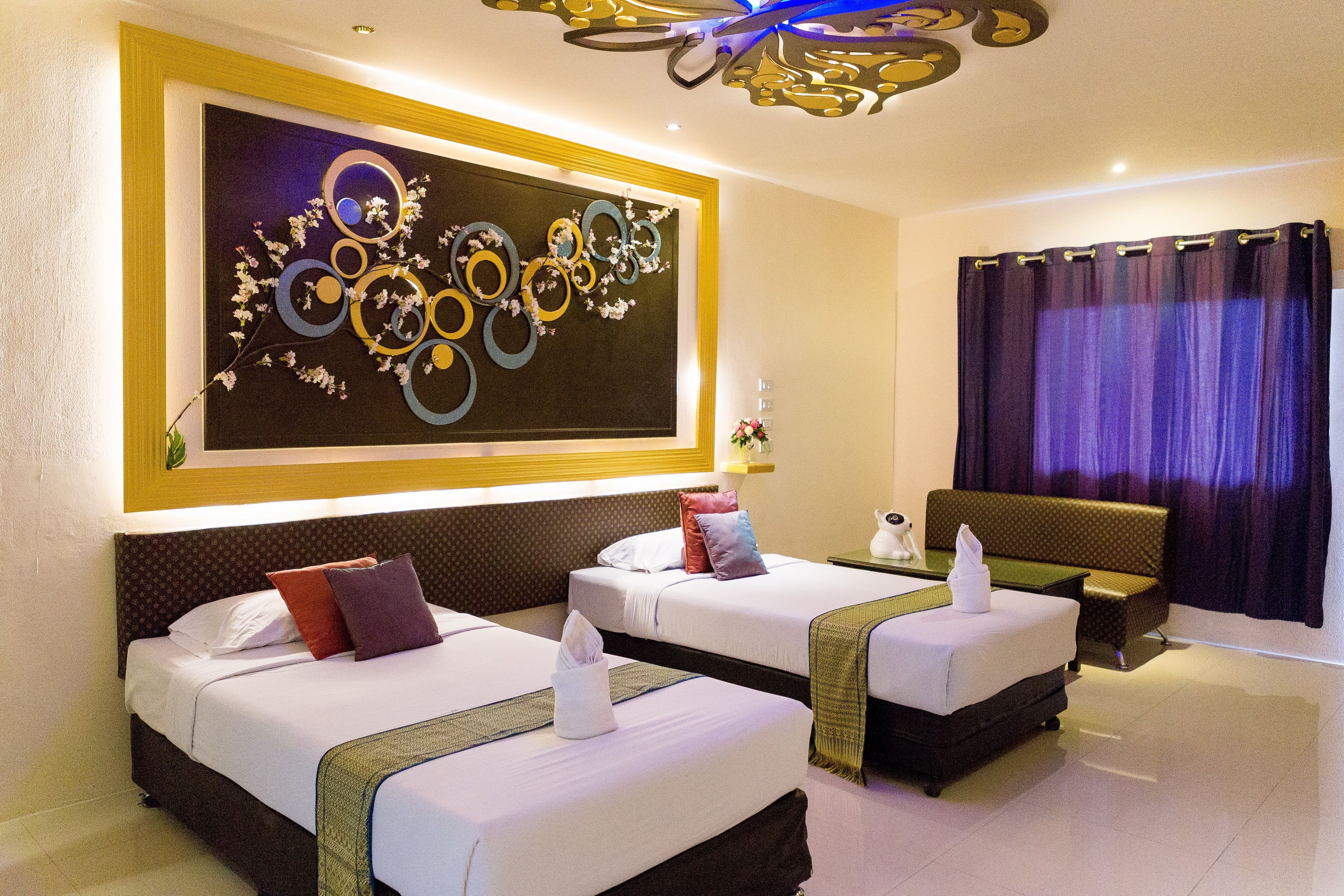 A hotel room with two beds, a large abstract painting on the wall, a modern chandelier, and a view of the city through the window.