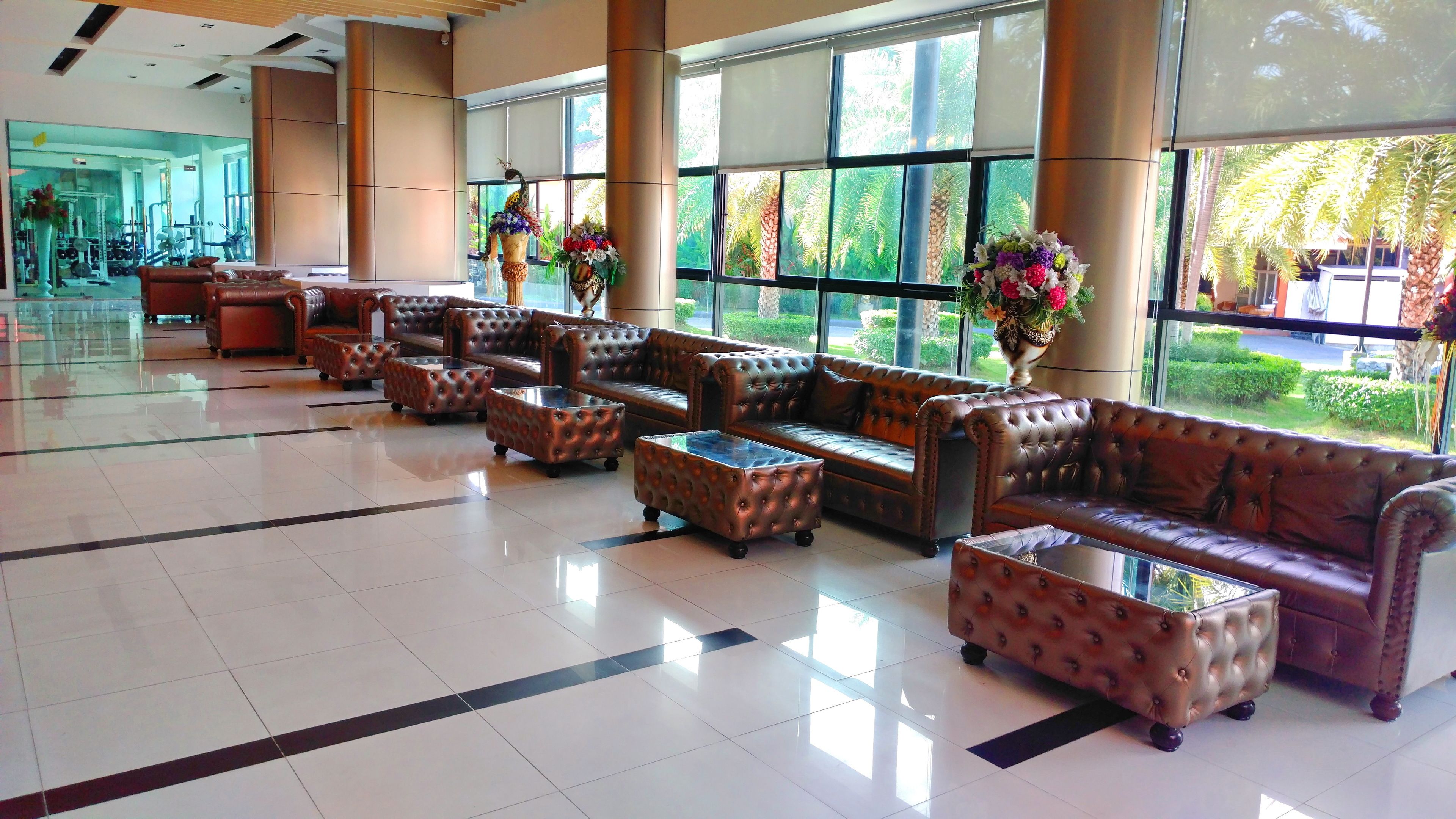 A spacious lobby with leather sofas and ottomans, large windows with a view of greenery, and a glass coffee table.