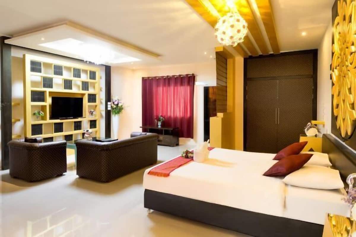 A modern hotel room with a large bed, a sofa, a TV, and a bookshelf.