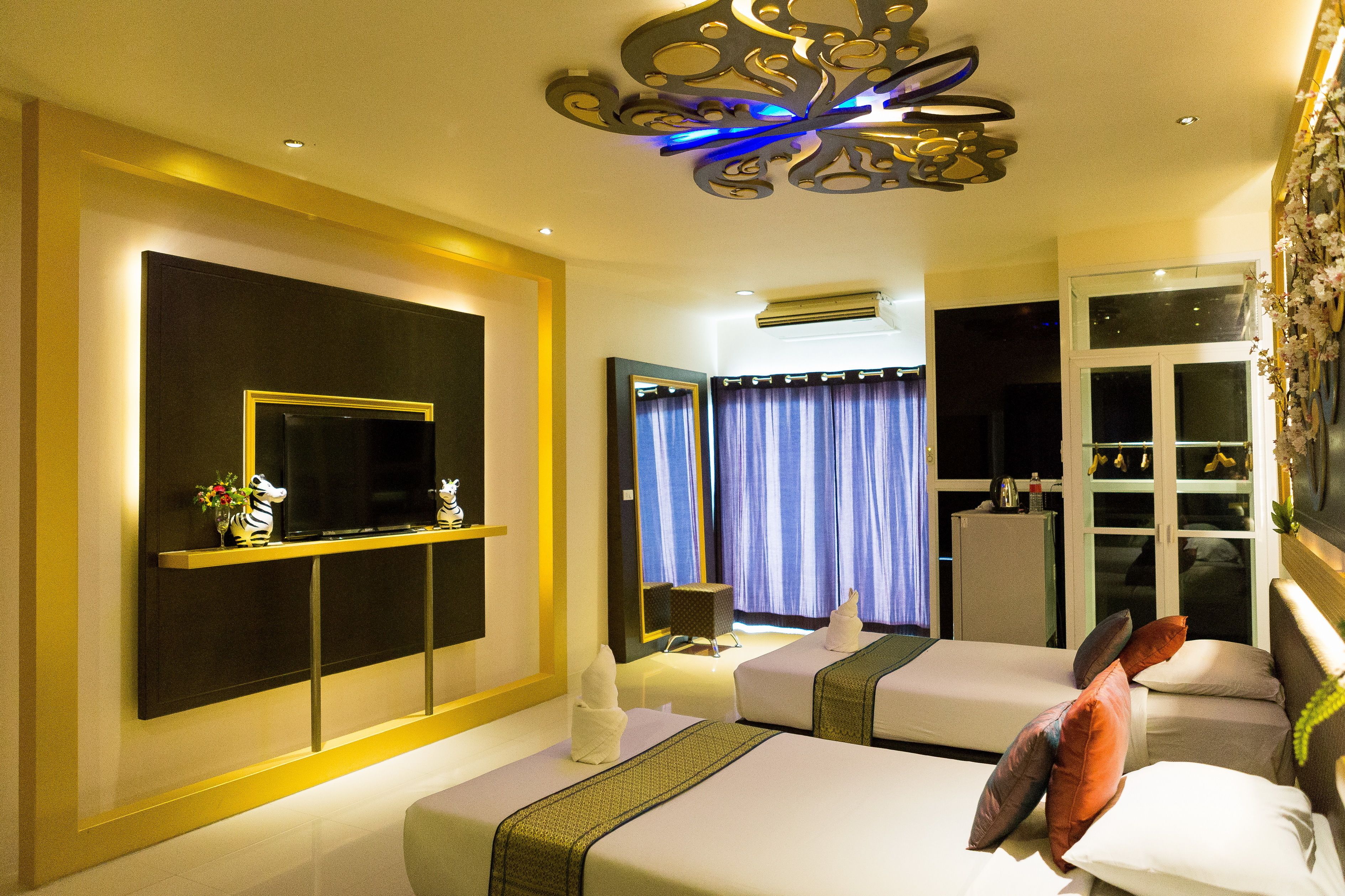 A hotel room with two beds, a flat-screen TV, a small table, and a decorative ceiling light.
