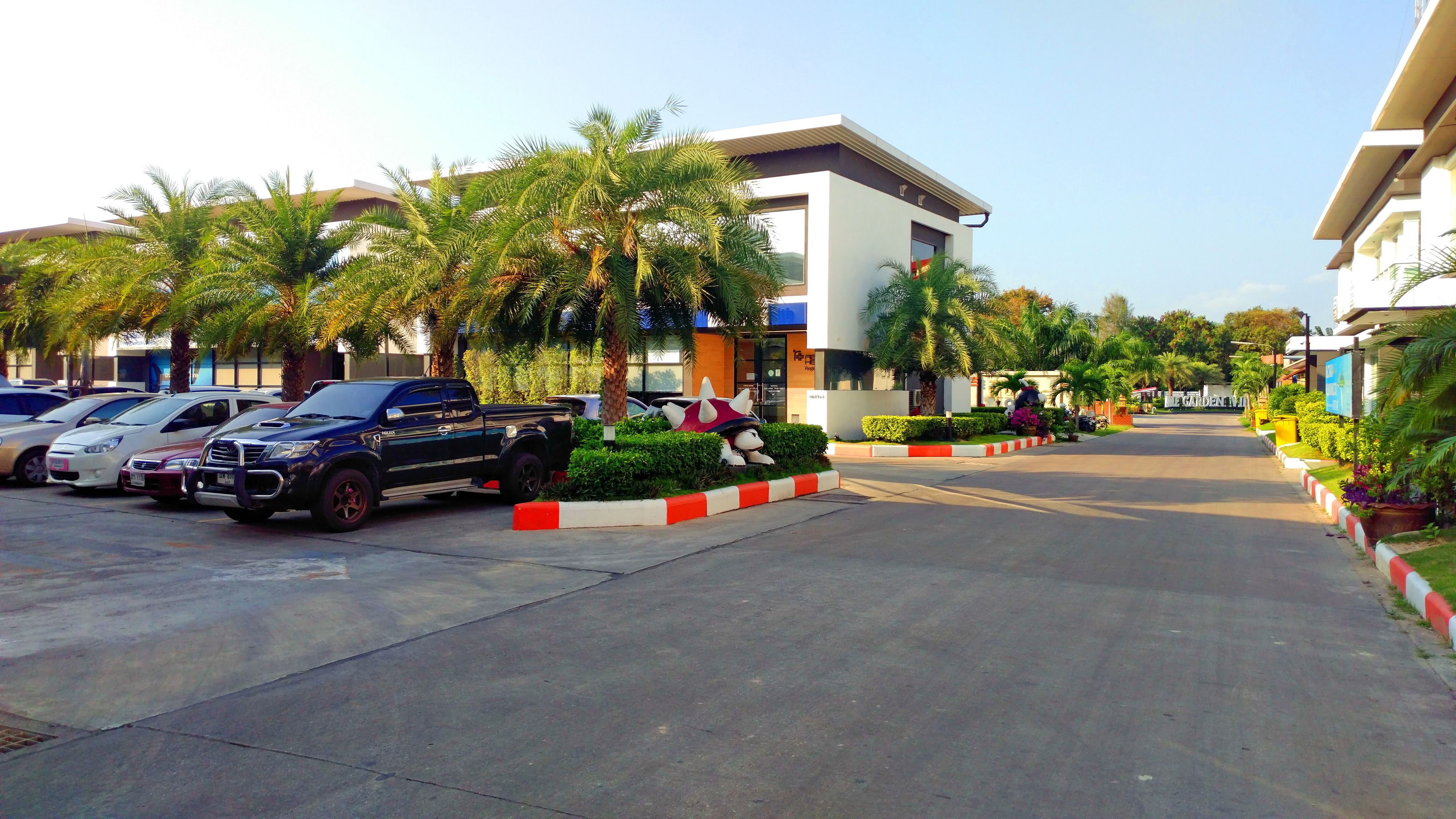 A parking lot with several cars, a modern building with a flat roof, and a statue of a dog wearing a crown.