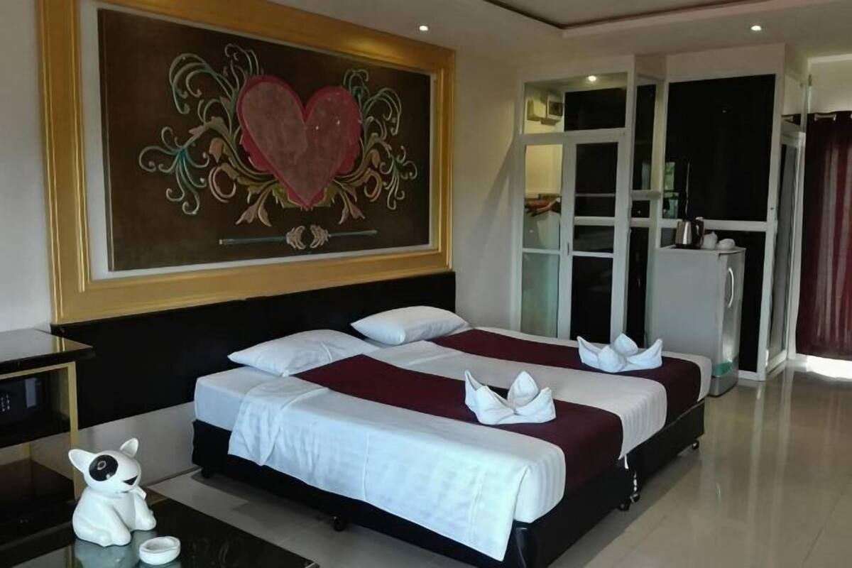 A hotel room with two beds, a large heart-themed painting, a minibar, and a view of a cityscape.