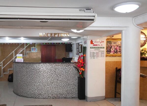 A reception area with a reception desk, air conditioning unit, and a sign indicating a prayer room. - Al-Sana Hotel (Bangkok)
