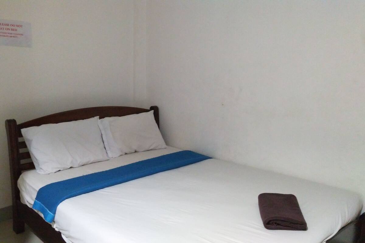A single bed with white bedding and a blue accent, a wooden headboard, and a folded brown towel on the footboard.