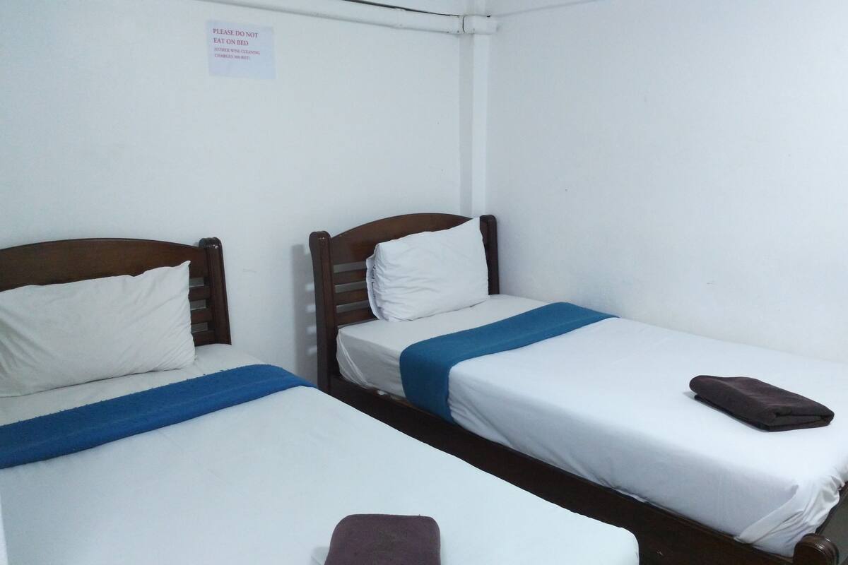 Two single beds with wooden headboards and white bedding, a sign prohibiting eating on the bed, and a blue towel on one bed.