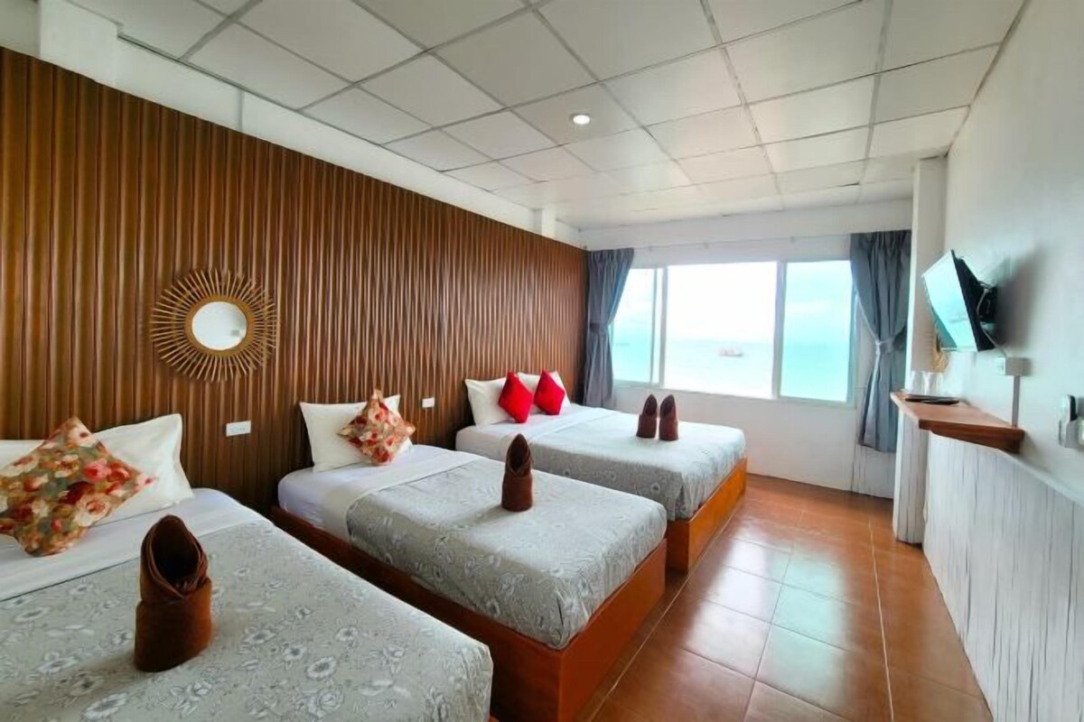 A hotel room with three beds, a TV on the wall, and a large window.