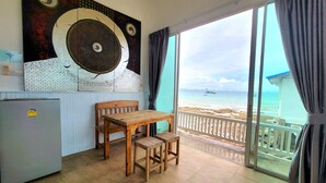 Una habitación con una mesa y sillas de madera, un refrigerador, un cuadro abstracto grande y vista a la playa y al océano a través de una puerta de vidrio.