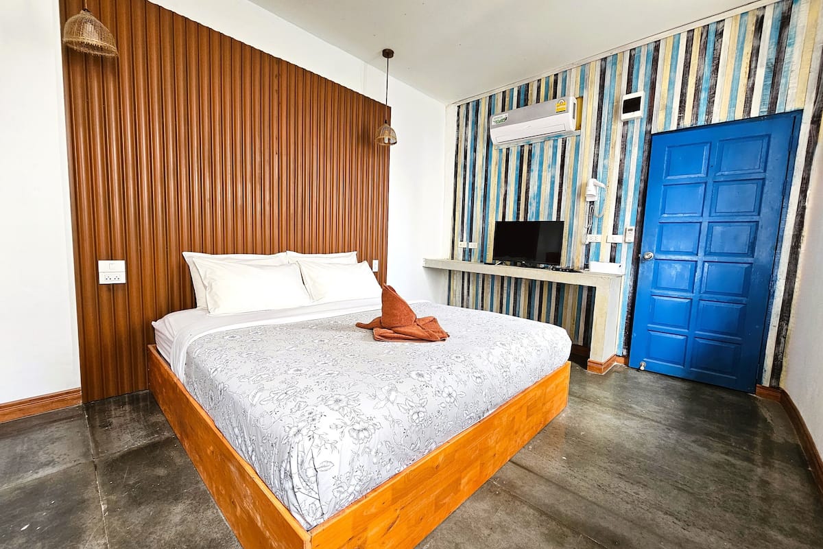A bedroom with a wooden headboard, a bed with floral bedding, a TV mounted on a wall, and a blue door.
