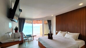 Habitación de hotel con una cama grande, un escritorio con computadora, un televisor montado en la pared y vista al océano a través de la puerta corrediza de vidrio.
