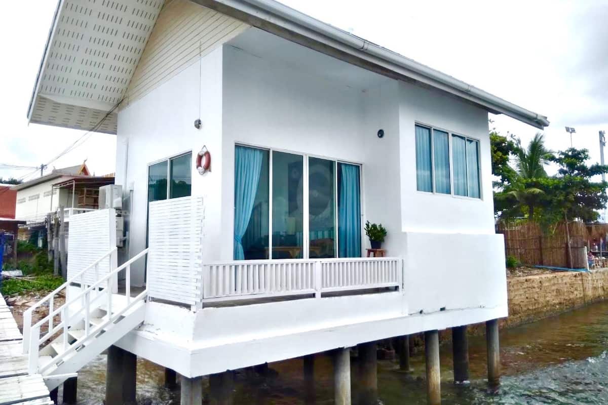 A white houseboat with a balcony, large windows, and a lifebuoy on the wall.