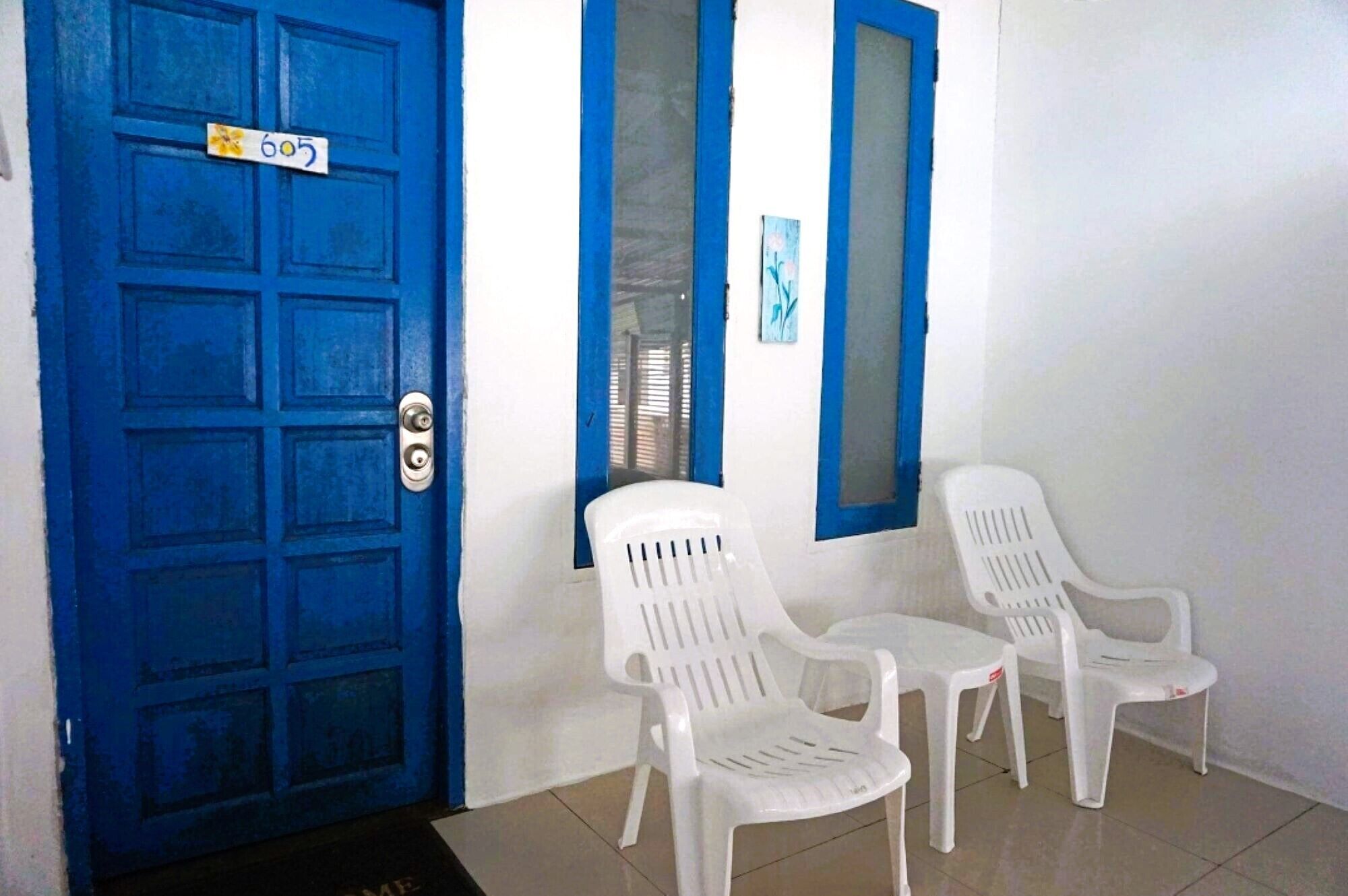 A blue door with a number plate, white walls, and two white plastic chairs.