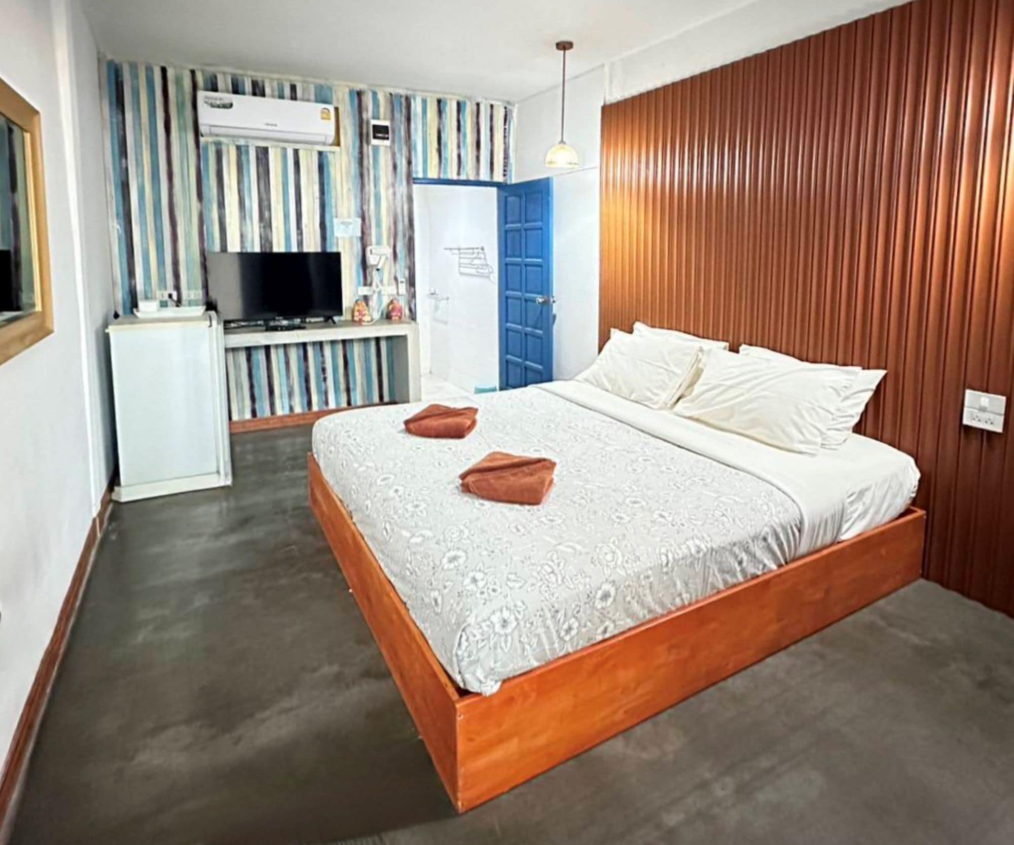 A bedroom with a wooden bed frame, a television, and a kitchenette area.