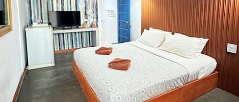 A bedroom with a wooden bed frame, a television, and a kitchenette area.